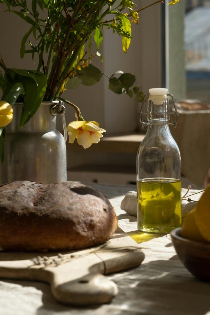 A serene kitchen setup featuring fresh bread, olive oil and flowers on a wooden table.